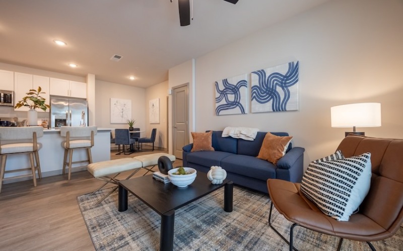 Stylish living room with blue sofa, leather chair, and open kitchen in the background.