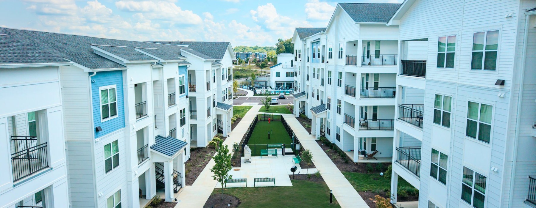 Modern apartment buildings facing a landscaped courtyard with walkways and green space.