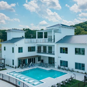 Settle into comfort at Madison Century Farms White clubhouse with outdoor pool and lounge chairs under a blue sky.