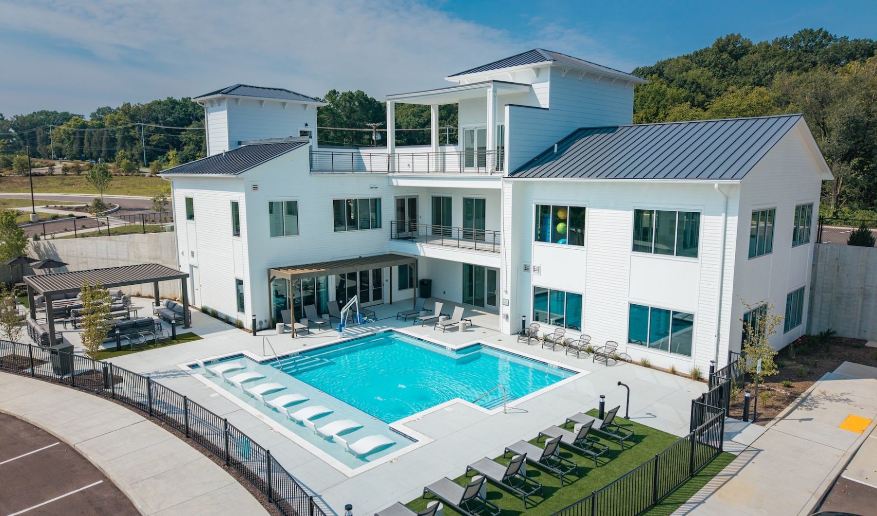 White modern clubhouse with outdoor pool, lounge chairs, and cabana seating on a sunny day.
